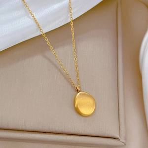 Macro shot of gold titanium necklace with engraved irregular bean pendant on beige fabric