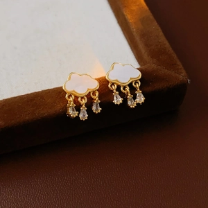 Close-up of golden cloud earrings with dangling zircon raindrops on a leather display