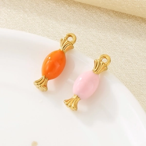 Detail of orange and pink enamel candy pendants with golden rings on a ceramic plate