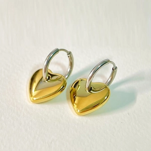 Macro shot of stylish gold and silver heart-shaped charm hoop earrings on grey background