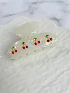 Close-up of white acetate hair claw clip with sparkling red cherry rhinestone designs