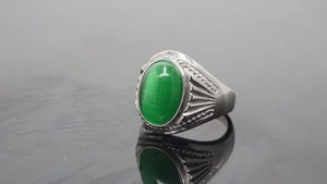 Close-up of a green cat's eye stone ring with engraved patterns on a polished metal band
