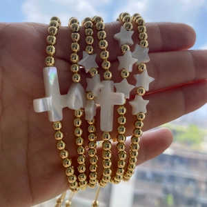 Detail of gold beaded bracelets with shell cross and star charms held in hand