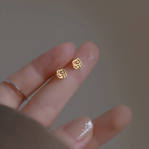 Macro shot of gold hollow rose stud earrings held on a finger showing petite size