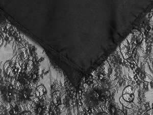 Detailed close-up of delicate floral lace trim on black satin dress hem with fine texture