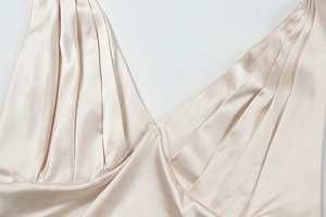 Detail des eleganten champagnerfarbenen Satinkleids mit tiefem V-Ausschnitt und Falten