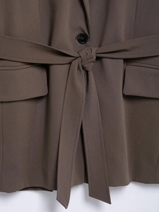 Close-up of brown blazer featuring a waist tie, single button, and flap pockets