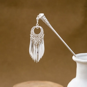 Detailed view of a silver tassel hairpin with hollow geometry in a white ceramic vase