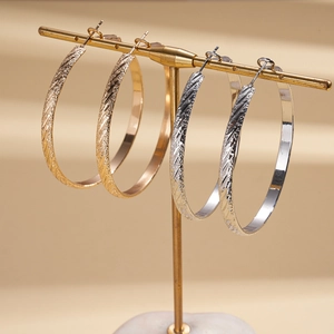 Elegant gold and silver geometric hoops with textured metallic twill design on stand