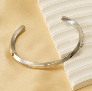 Macro detail of silver twisted C-shape stainless steel bracelet on a minimalist display