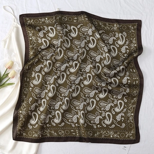 Detail of olive green paisley silk scarf elegantly folded on white textured bedding