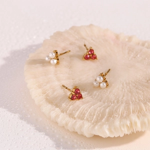 Detail of gold clover earrings with red gemstones and white pearls on white coral