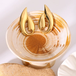 Polished golden geometric titanium steel earrings on a ceramic dish with stone accents