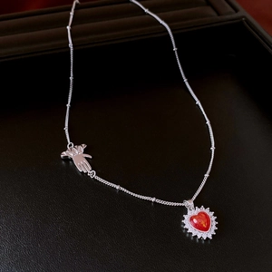 Macro detail of silver necklace with red heart pendant and palm charm on black tray