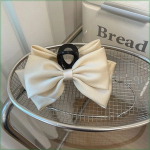 Close-up of a large cream satin bow hair claw clip placed in a silver metal basket
