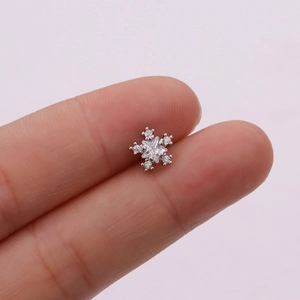 Macro view of silver snowflake stud earring with clear zircon inlay on a fingertip