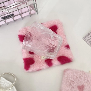 Close-up of a pink plush square coaster with heart pattern and textured glass water cup