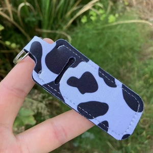 Detail of cow print lipstick holder with metal keyring on a natural grass background