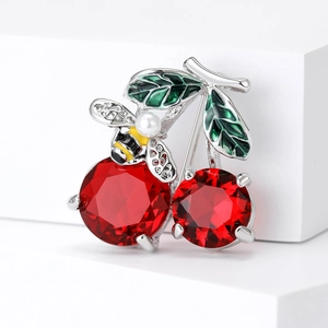 Elegant crystal cherry brooch with bee detail and green enamel leaves on white pedestal