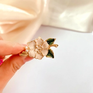 Macro detail of enamel poppy flower brooch with pink petals, green leaves and pearls