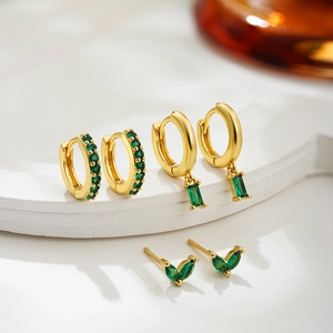 Detail of 18K gold earrings set with emerald green zircons on a white display