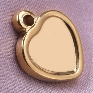 Detailed view of a polished gold heart-shaped pendant on textured pink fabric background