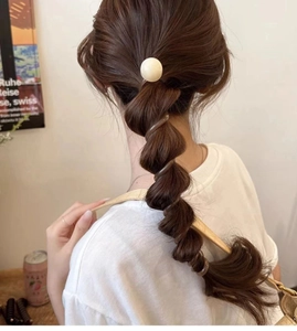 Close-up of a brown spiral hair tie with a cream bead detail on a woman's ponytail