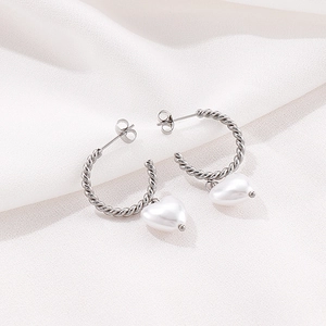 Vue macro de boucles d'oreilles créoles torsadées avec pendentifs perles cœur blanc