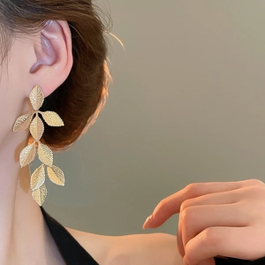 Close-up of elegant gold leaf tassel earrings worn by a model for a luxury style