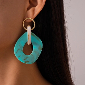 Close-up of model wearing irregular hollow geometric earrings with blue marble texture