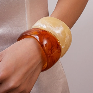 Detail view of wide resin bangles in amber tortoise and cream marble pattern textures