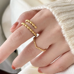 Detailed view of gold beaded stackable rings worn over a cream knit sweater background