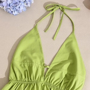 Flat lay detail of a green halter neck dress with ties on a sandy beach background