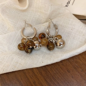Macro detail of bead earrings featuring amber resin and metallic spheres on fabric