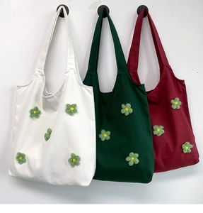 Detailed view of canvas tote bags in white, dark green, and red with knitted flower charms
