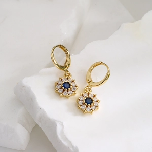 Gold-plated floral earrings with blue zircon center and white gemstones on white stone