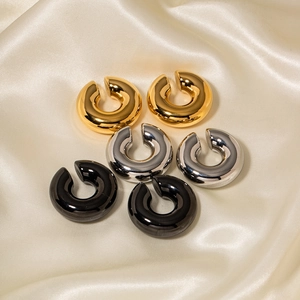 Détails des boucles d'oreilles créoles C en or, argent et noir sur un tissu en soie douce