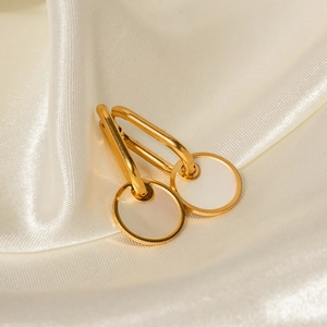 Close-up of golden titanium earrings with white round mother of pearl pendants on silk