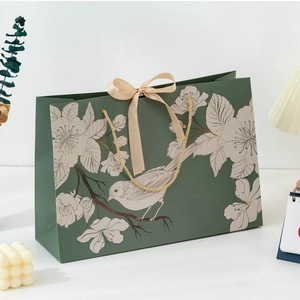 Dark green paper gift bag with white floral pattern, beige ribbon bow and gold handles