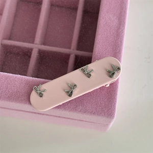 Close-up of pink bow hair clip with four silver metal butterfly ornaments on a jewelry box