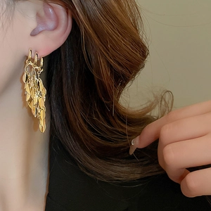 Close-up of golden three-layer geometric tassel earrings worn by a model in soft light