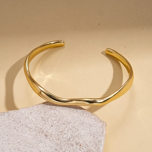 Detailed view of 18k gold plated wavy open cuff bracelet on a minimalist stone display