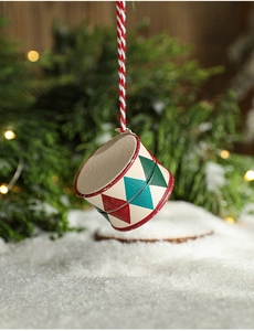 Detail of a vintage hand-painted metal drum ornament on a snowy Christmas tree branch