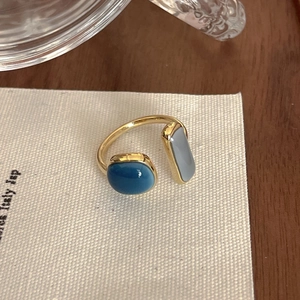 Detail shot of golden open ring with blue round stone and grey rectangular gem on textured paper