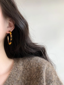 Close-up of amber tortoiseshell resin C-shaped hoop earrings on model's ear