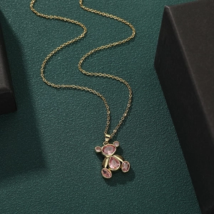 Exquisite gold-plated teddy bear necklace with pink gemstone pendant on green surface