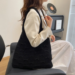 Detail of a black knitted shoulder bag with a textured diamond pattern on the surface