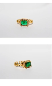 Macro detail of gold chain ring featuring emerald cut green stone and diamond halo