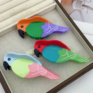 Drei farbenfrohe Haarklammern in Papageienform aus Acetat in einem eleganten Holztablett