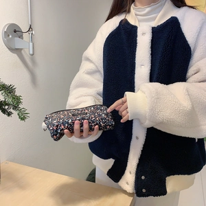 Detail of dark floral corduroy pouch held by a model wearing a lamb wool jacket